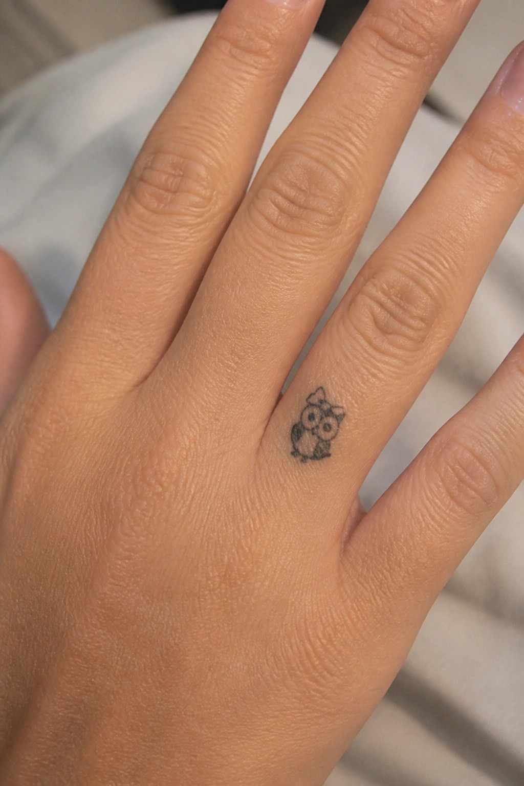 Small black ink owl tattoo with a bow on the side of a finger