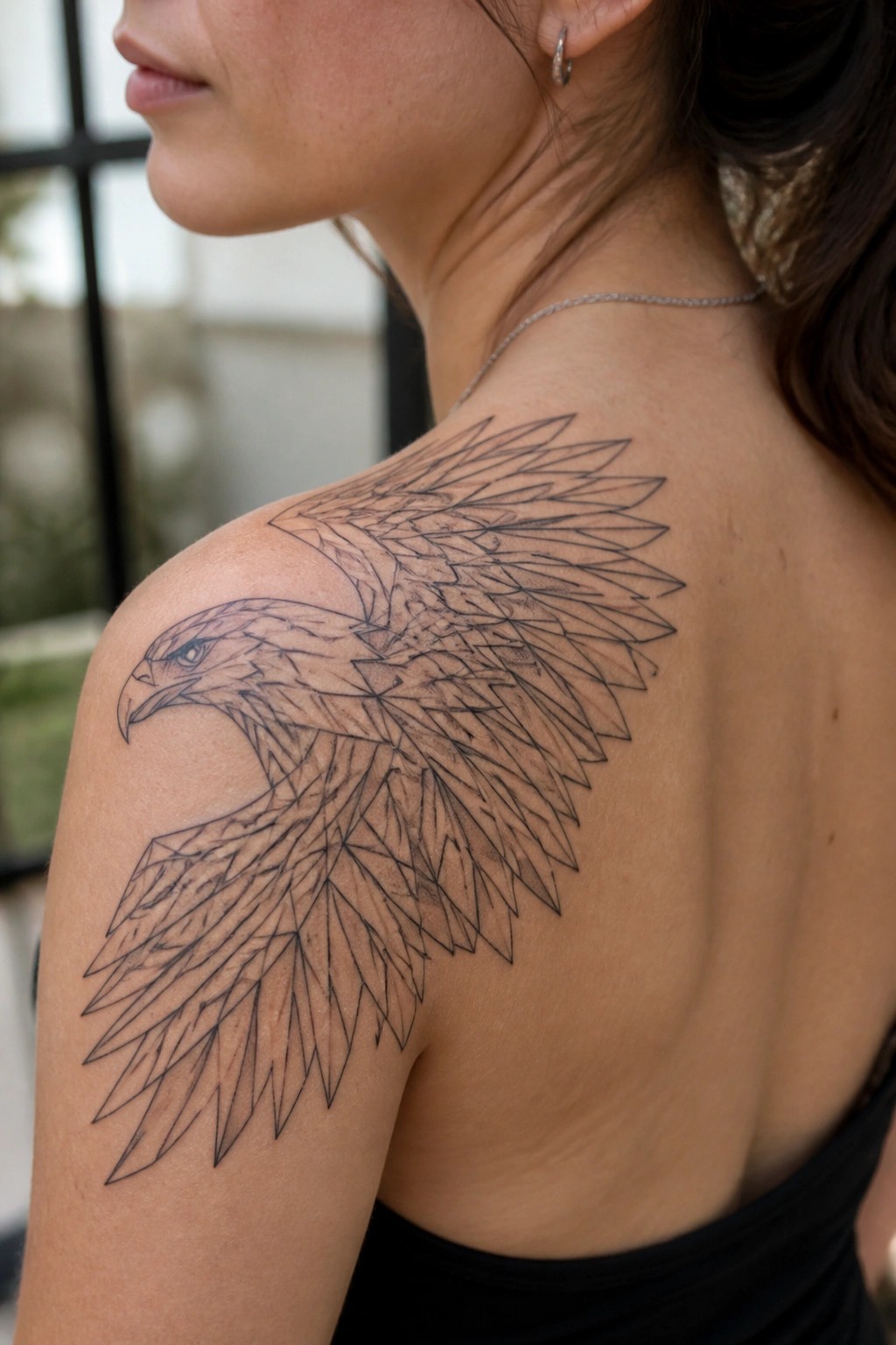 Woman's shoulder and back with large geometric eagle tattoo in black ink