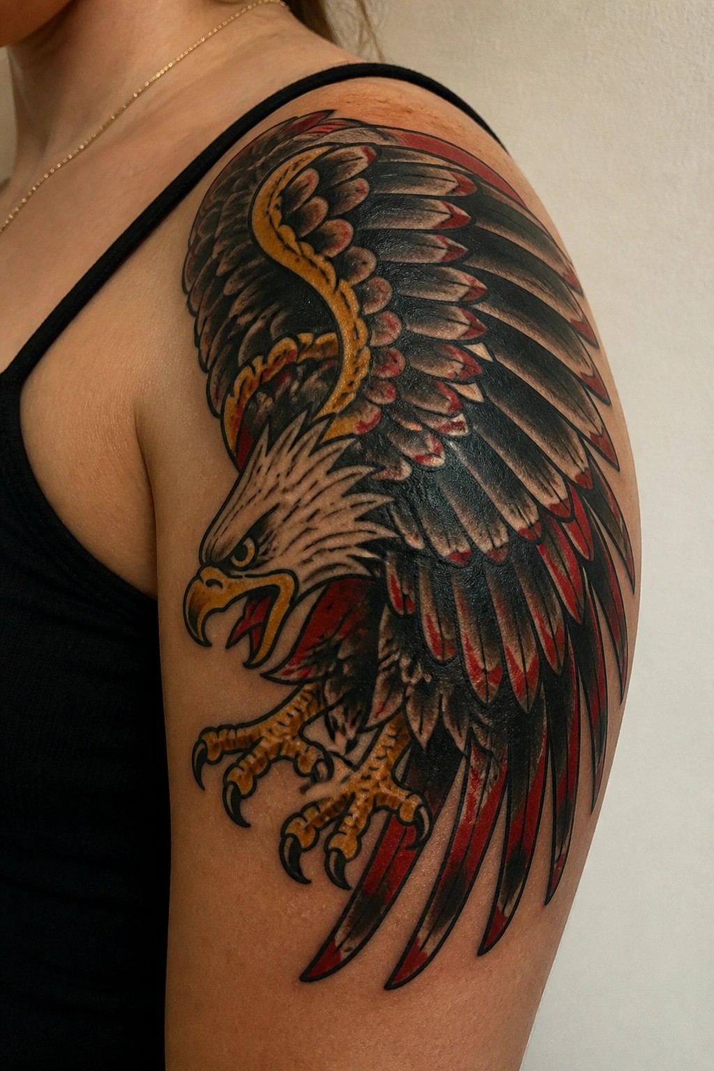 Colorful traditional eagle tattoo on shoulder above black tank top with gold necklace