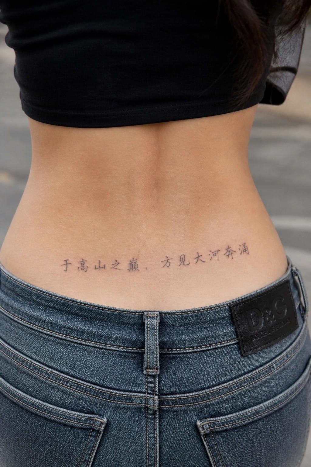 Lower back Chinese tattoo above blue D&G jeans and black crop top