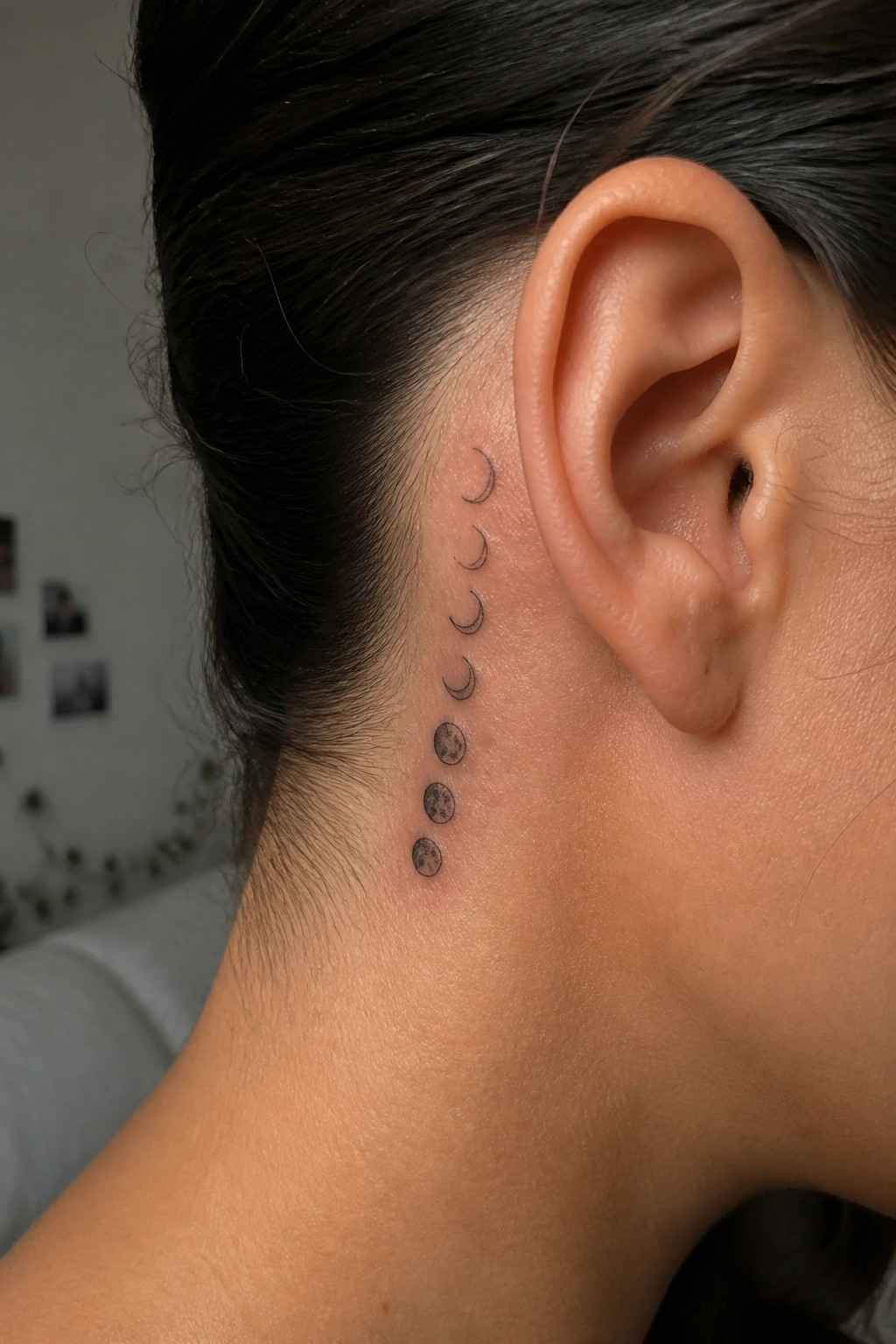 Vertical moon phase tattoo behind the ear showing progression from crescent to full moons in minimalist style.