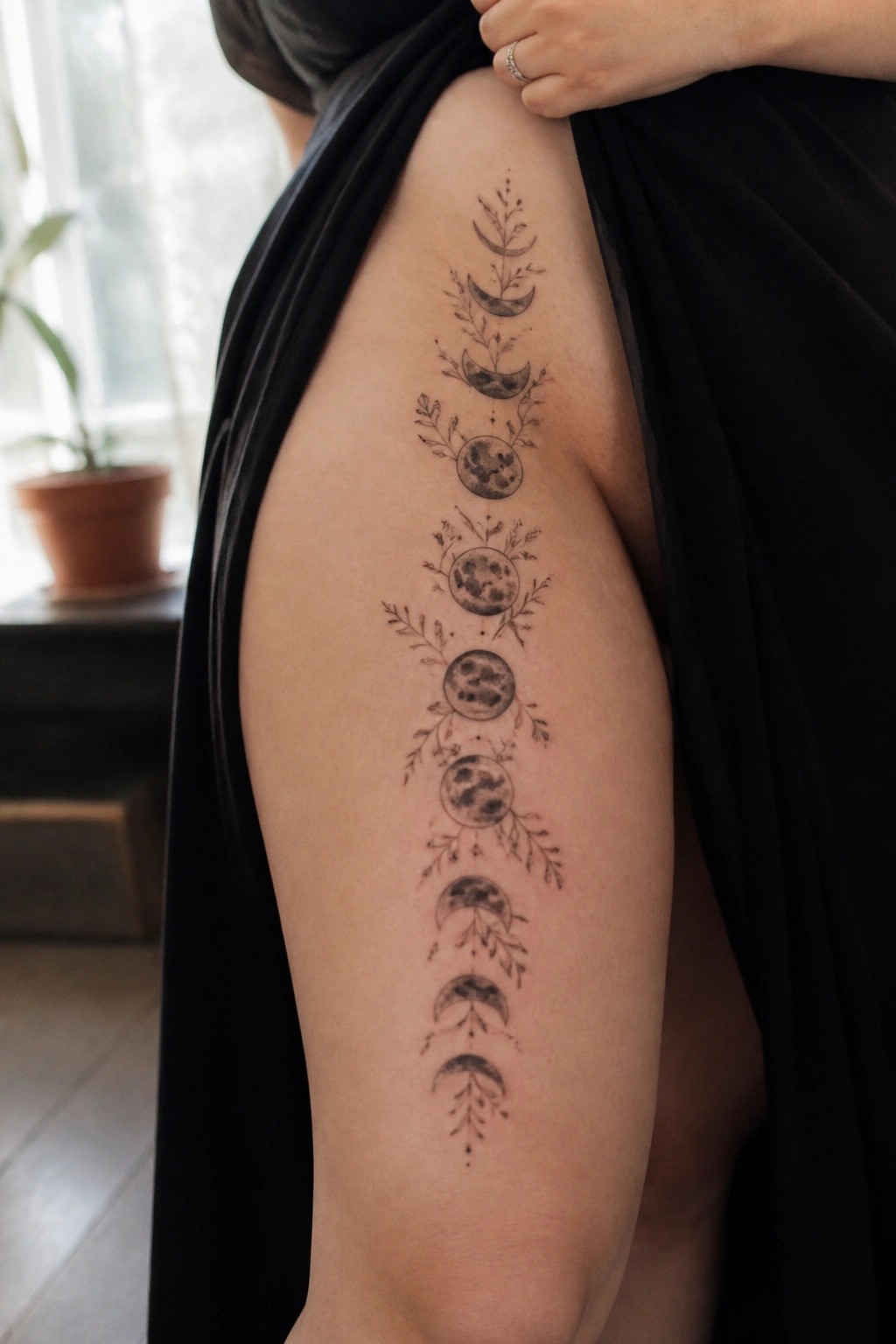 Vertical moon phase tattoo on the thigh showing the full lunar cycle with delicate botanical accents in black ink