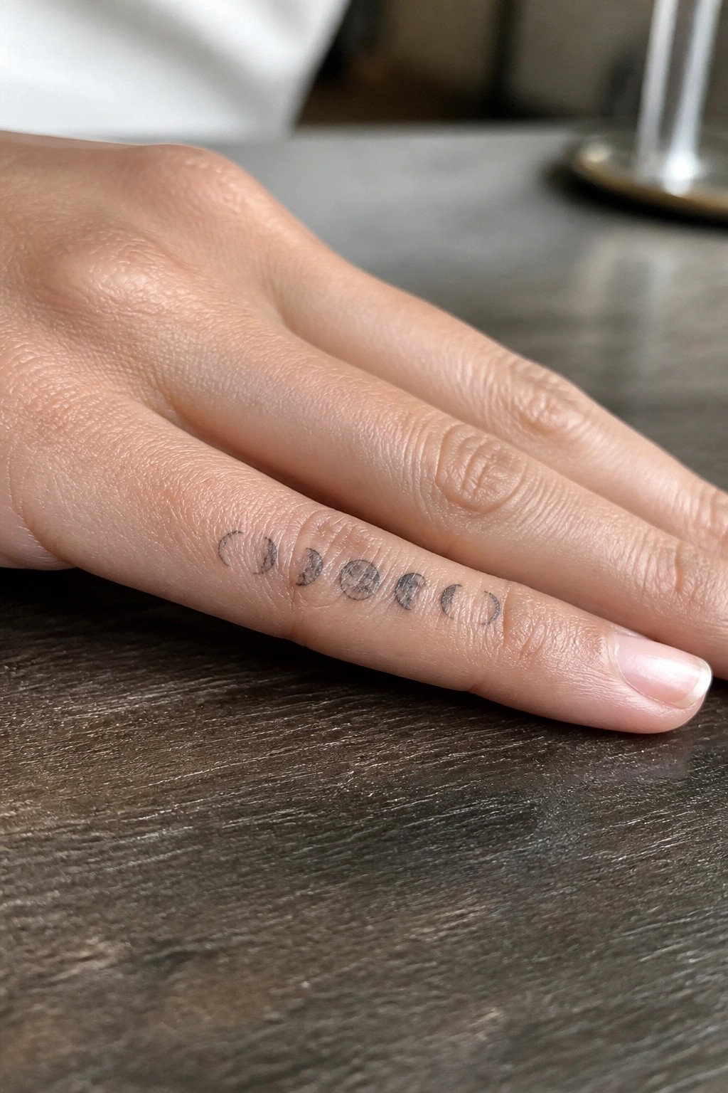 Moon phase tattoo in a horizontal row on the side of a finger showing the full lunar cycle in black ink