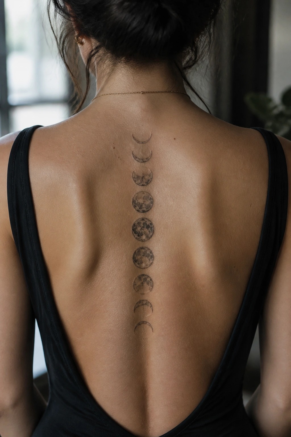 Vertical row of moon phase tattoos centered along a woman's upper back spine in black ink.