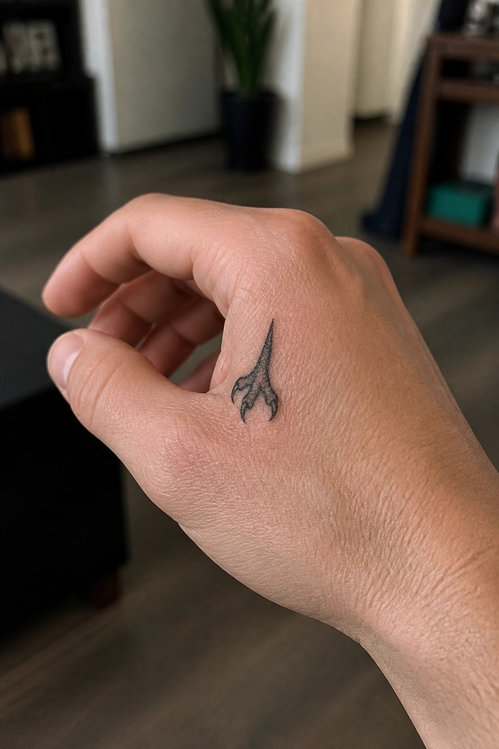 Light-skinned hand with small black bird claw tattoo near thumb knuckle