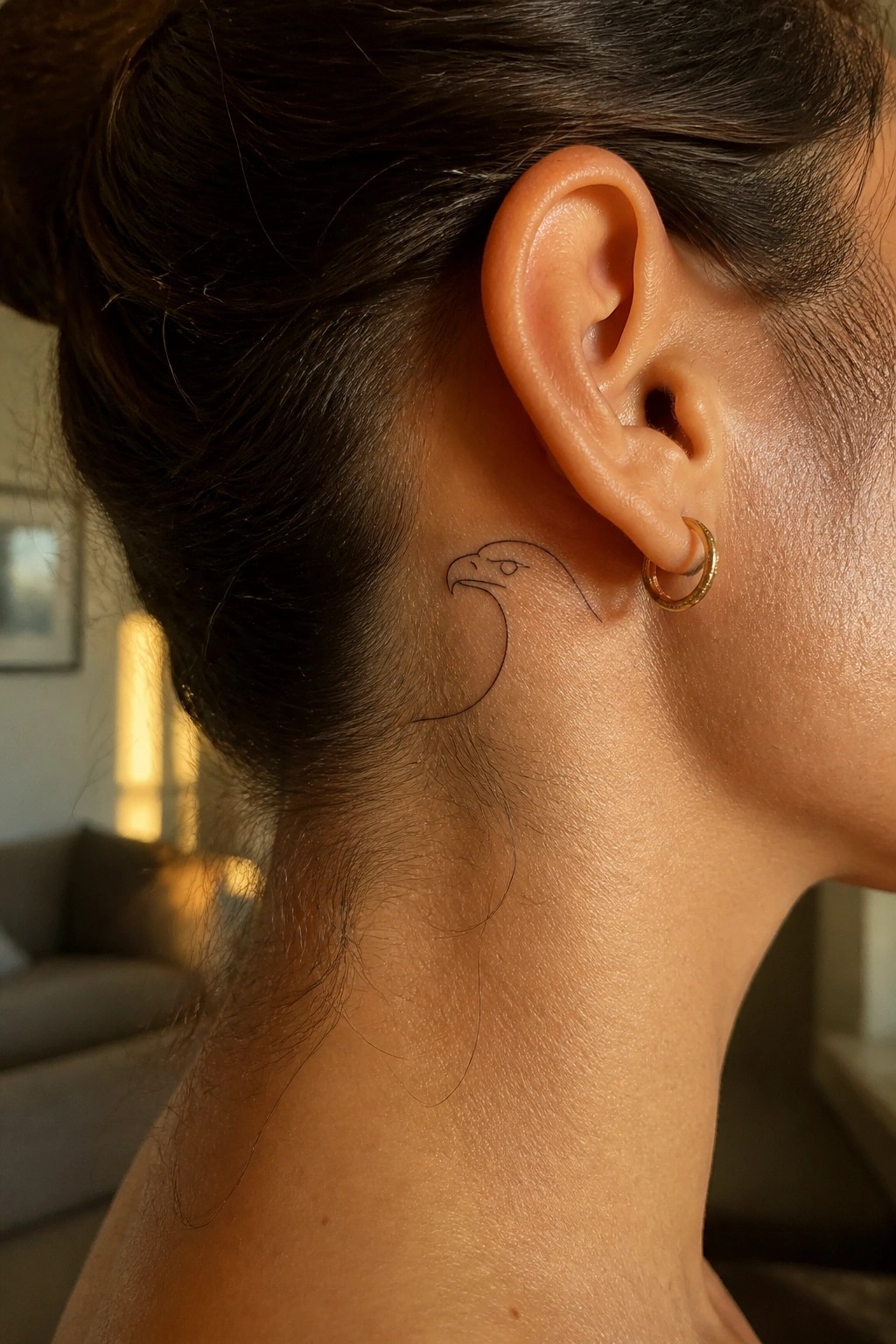 Woman's neck with eagle tattoo behind ear and small gold hoop earring