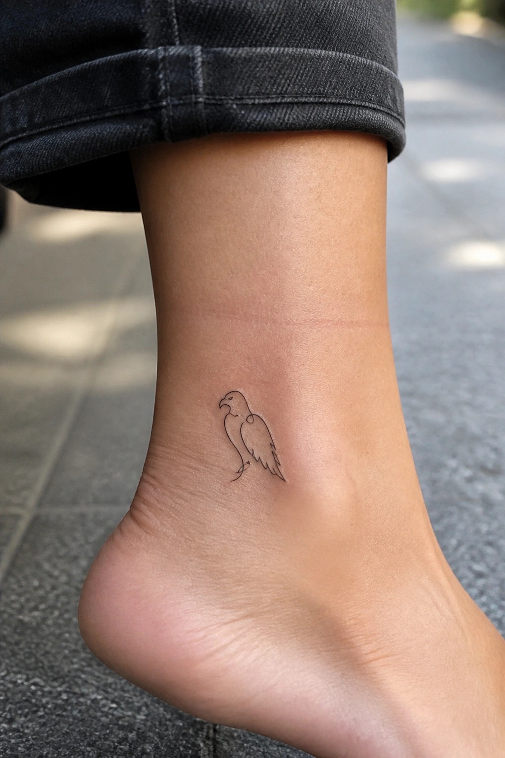 Minimalist line drawing of a small eagle tattoo on the outer ankle.