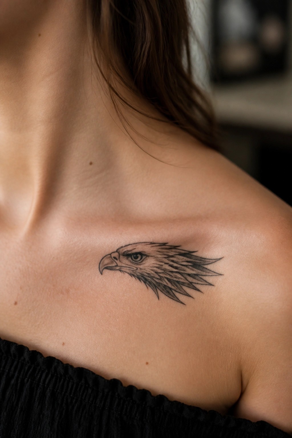 Detailed black eagle head tattoo on light-skinned shoulder above black off-shoulder top
