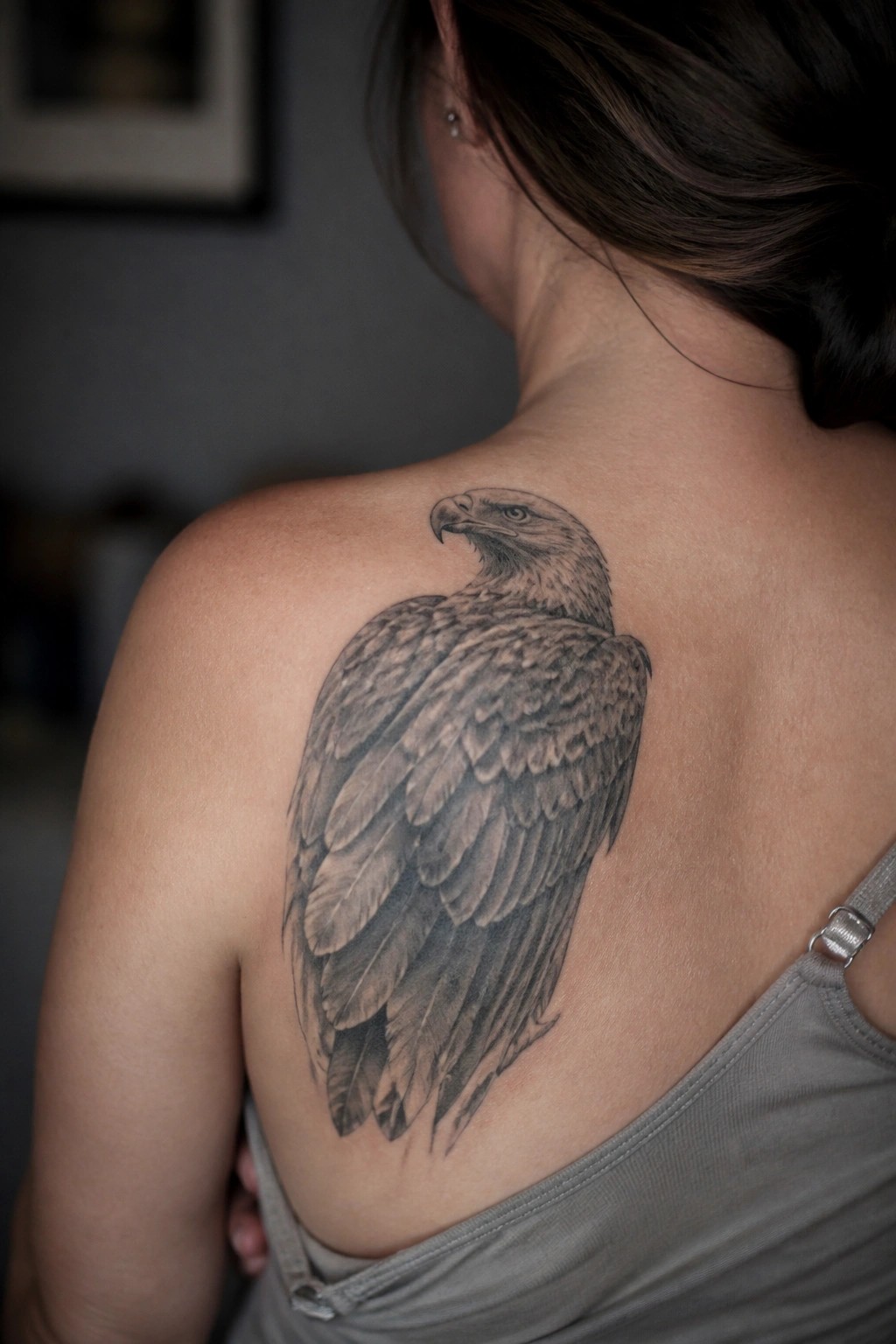 Detailed eagle tattoo on woman's upper back over gray tank top