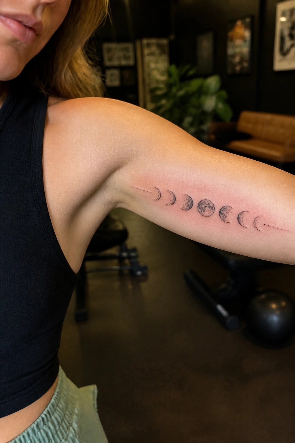 Horizontal moon phases tattoo on a woman's upper arm showing the lunar cycle in fine black ink.