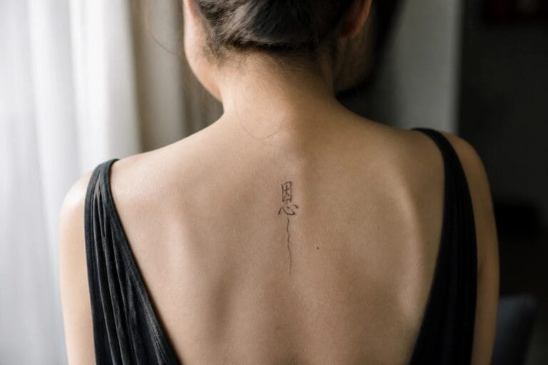 19 Chinese Spine Tattoo Ideas for Women With Graceful Vertical Flow Woman's bare back in black dress with vertical Chinese tattoo and hair bun