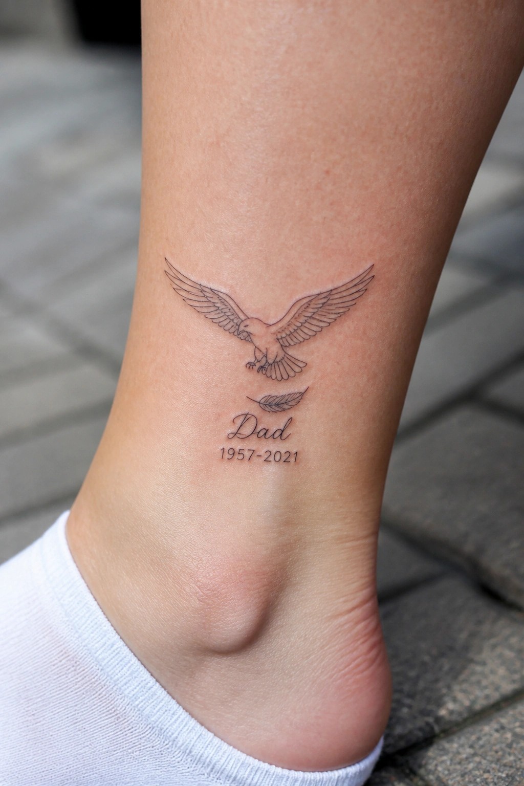 Minimalist line art eagle tattoo on the ankle with Dad and memorial dates below it.