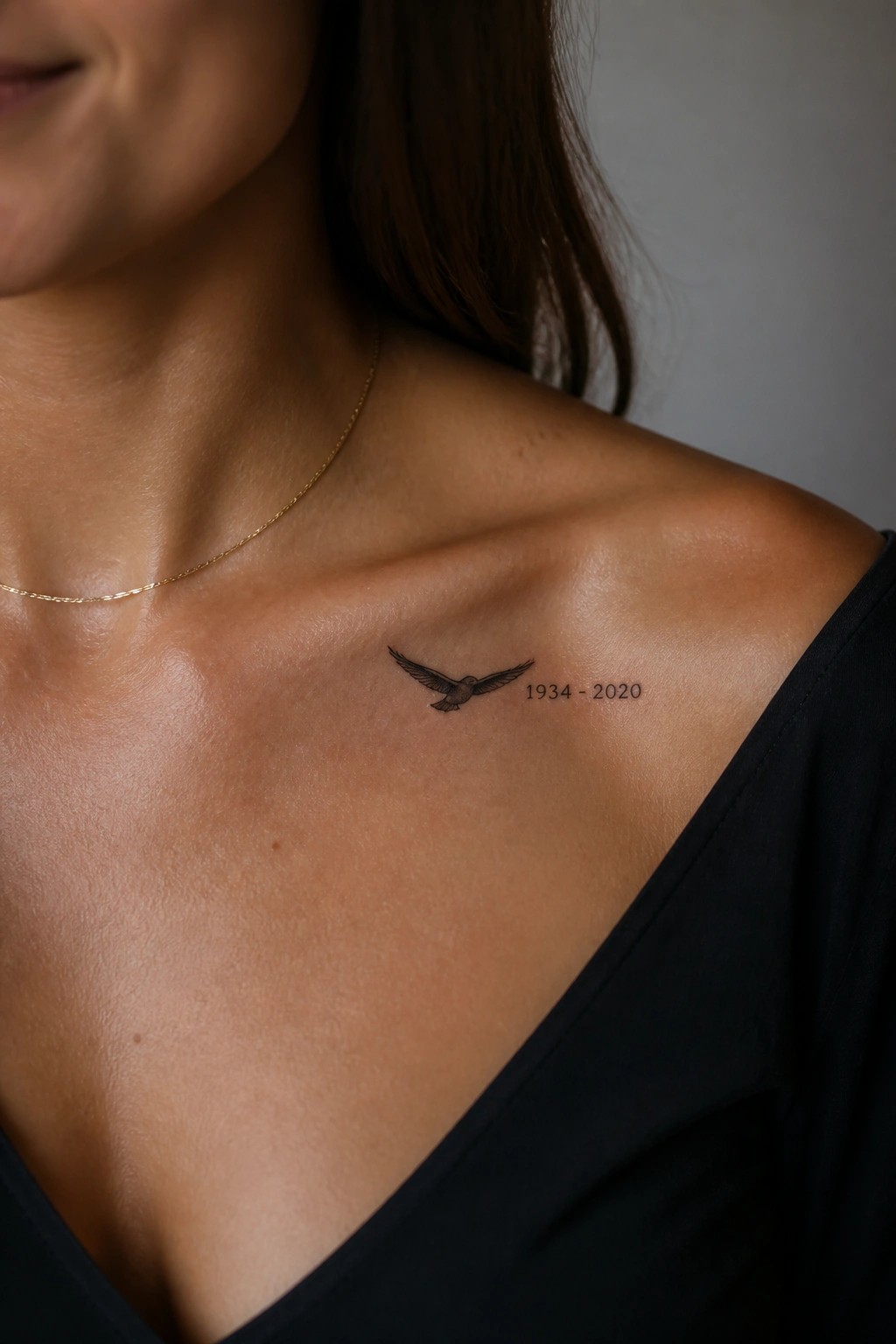 Small flying bird tattoo with dates on a woman's collarbone area