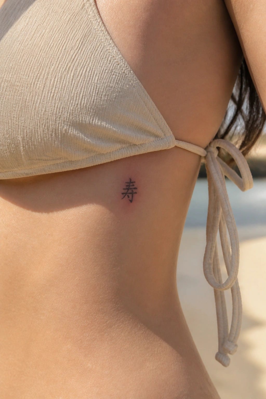 Beige bikini top with small black Chinese character tattoo on side at beach.