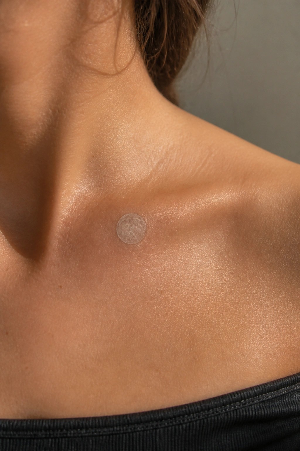 Small shaded full moon tattoo on the upper chest below the collarbone