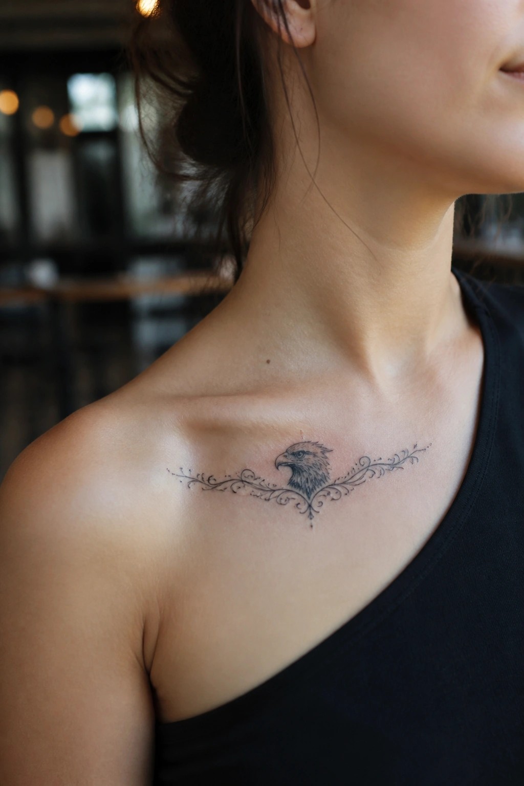 Fine line eagle head tattoo with decorative swirls on the collarbone area