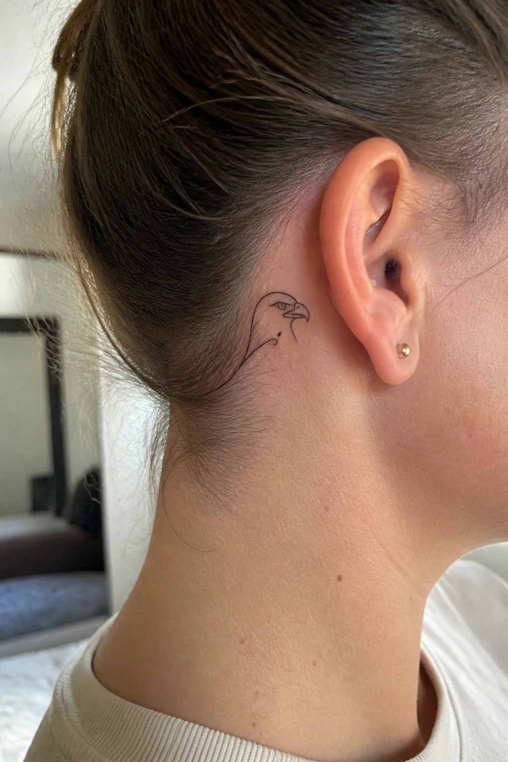 Fine line eagle head tattoo placed behind the ear on the side of the neck