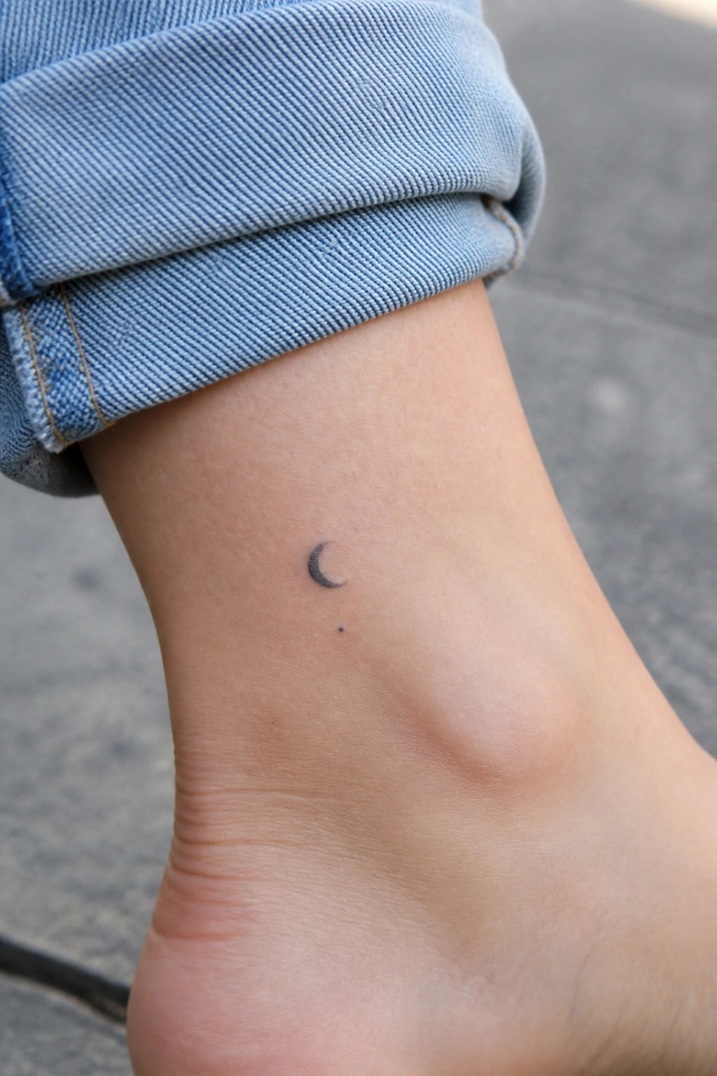 Rolled-up blue jeans on ankle with small crescent moon and dot tattoo