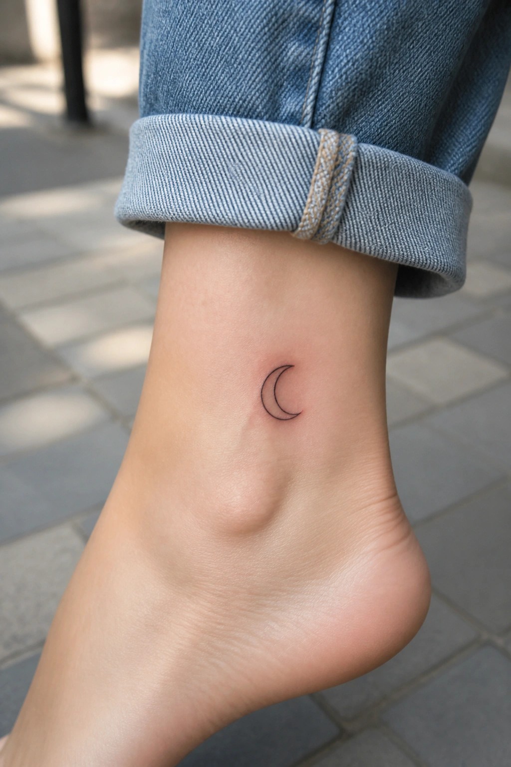 Small black linework crescent moon tattoo on the ankle above the foot.