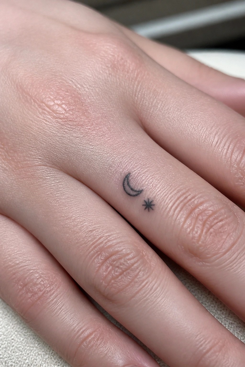 Close-up of light-skinned hand with small black crescent moon and star tattoo on finger.