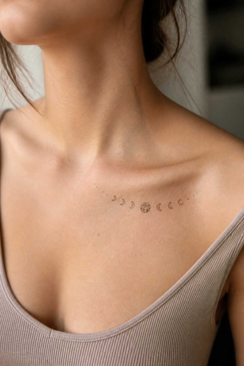 Moon phase tattoo across collarbone above beige ribbed tank top