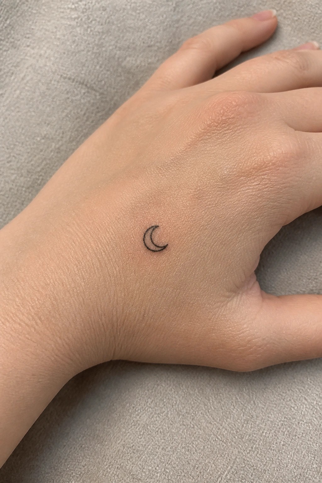Small black line crescent moon tattoo on the back of a hand