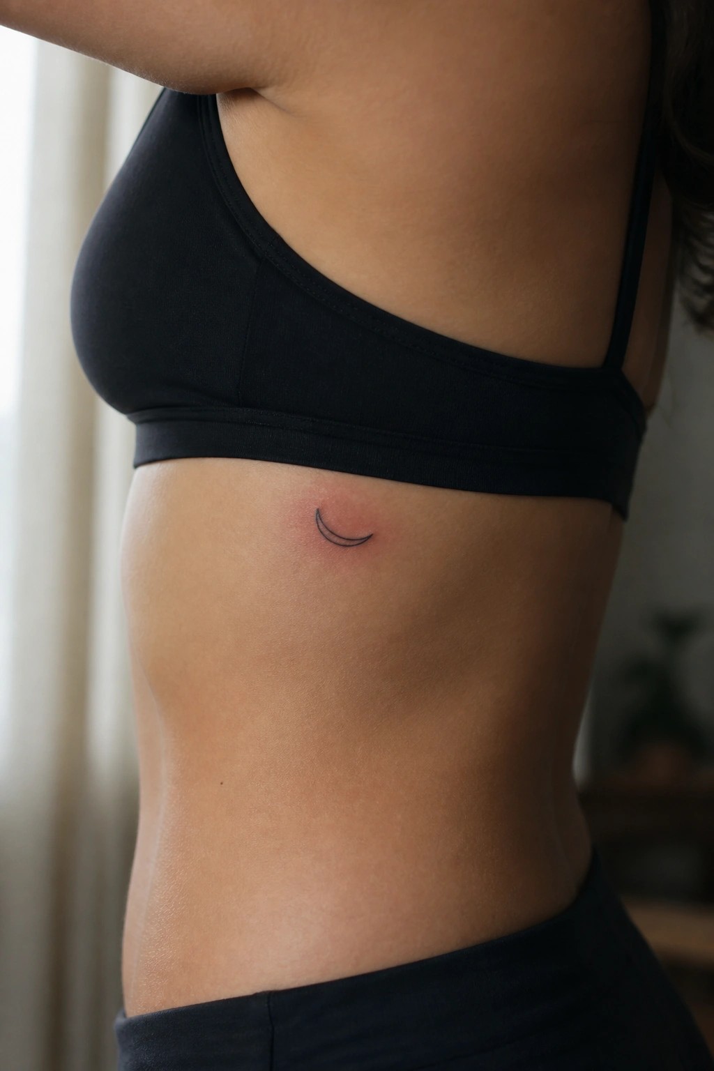 Torso in black sports bra with small crescent moon tattoo and redness.
