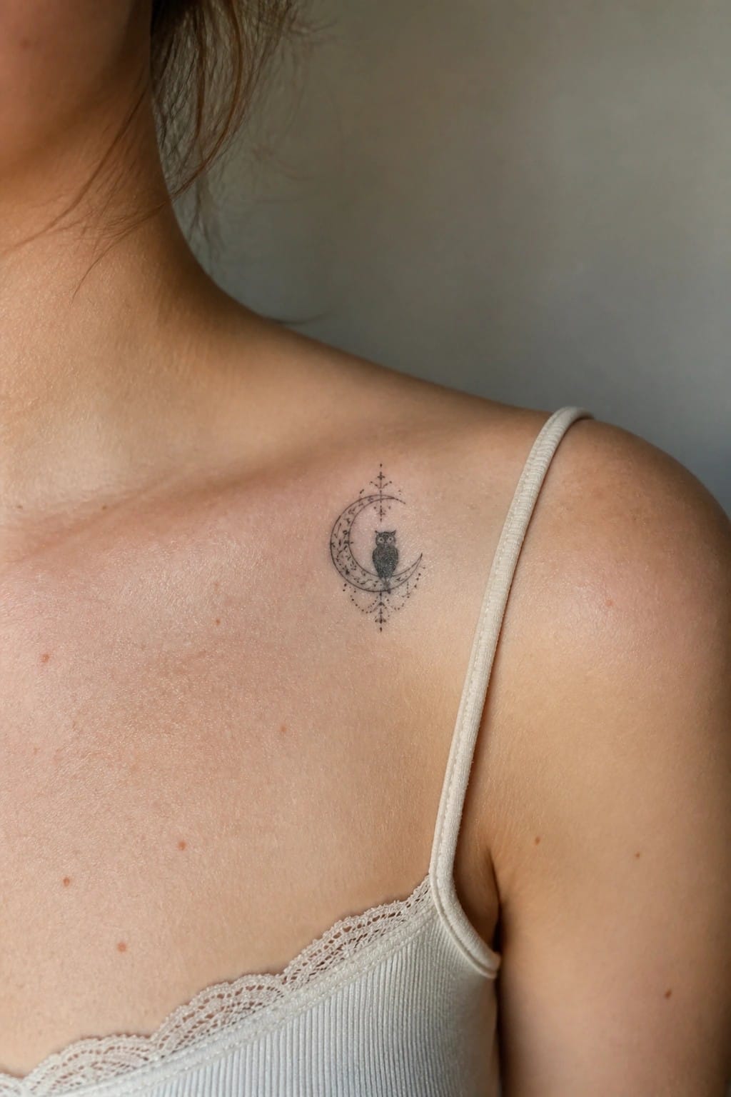 Fine line tattoo of an owl on a crescent moon placed on the upper shoulder near the collarbone