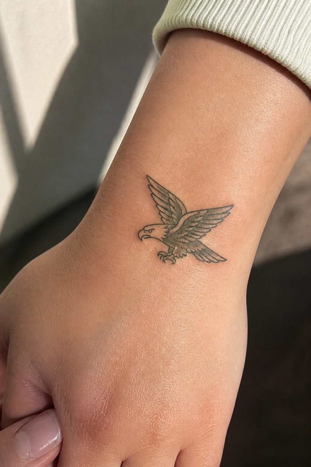 Small fine line eagle tattoo in flight on the inner wrist of a woman.