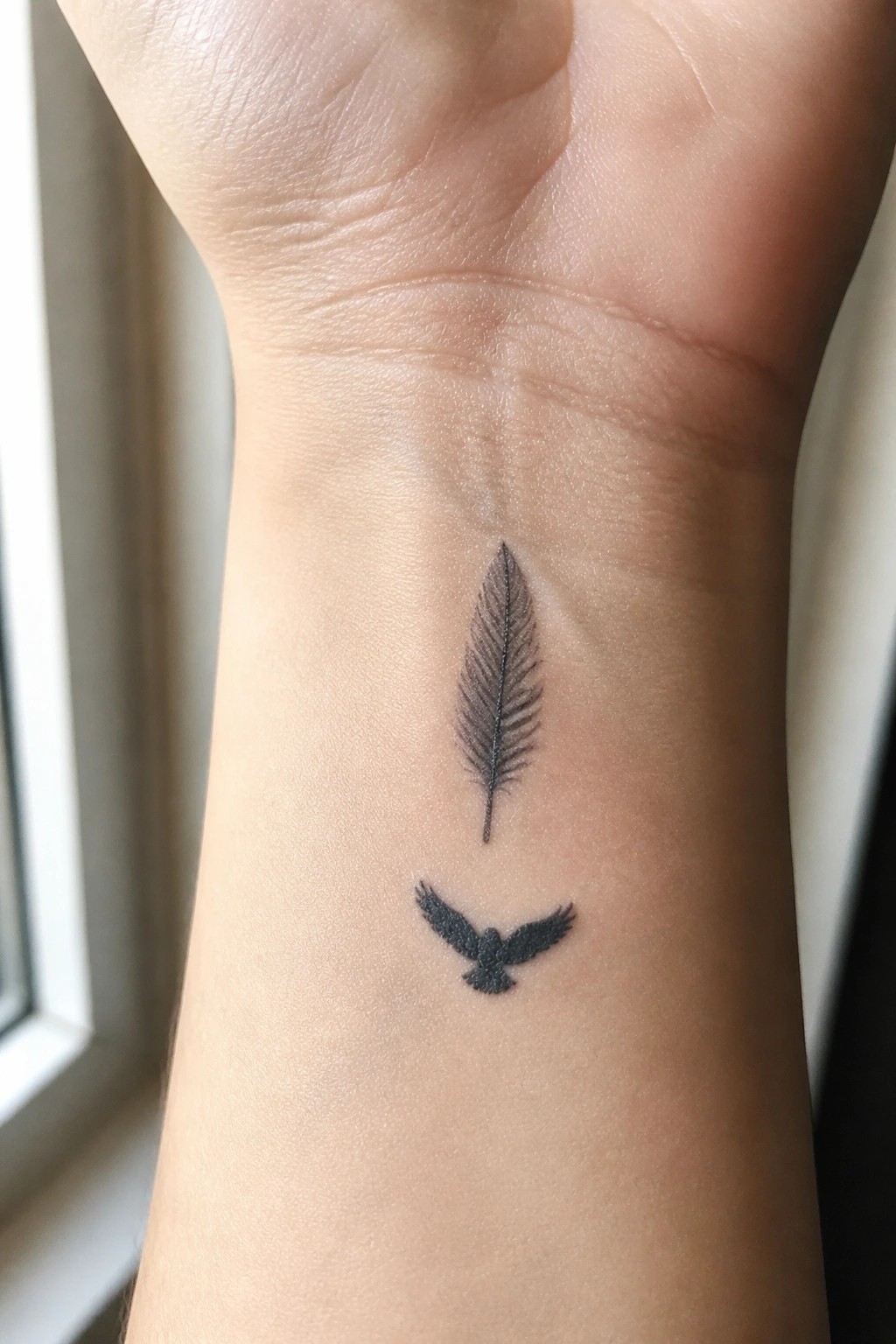 Black feather and flying bird tattoos on light-skinned inner wrist