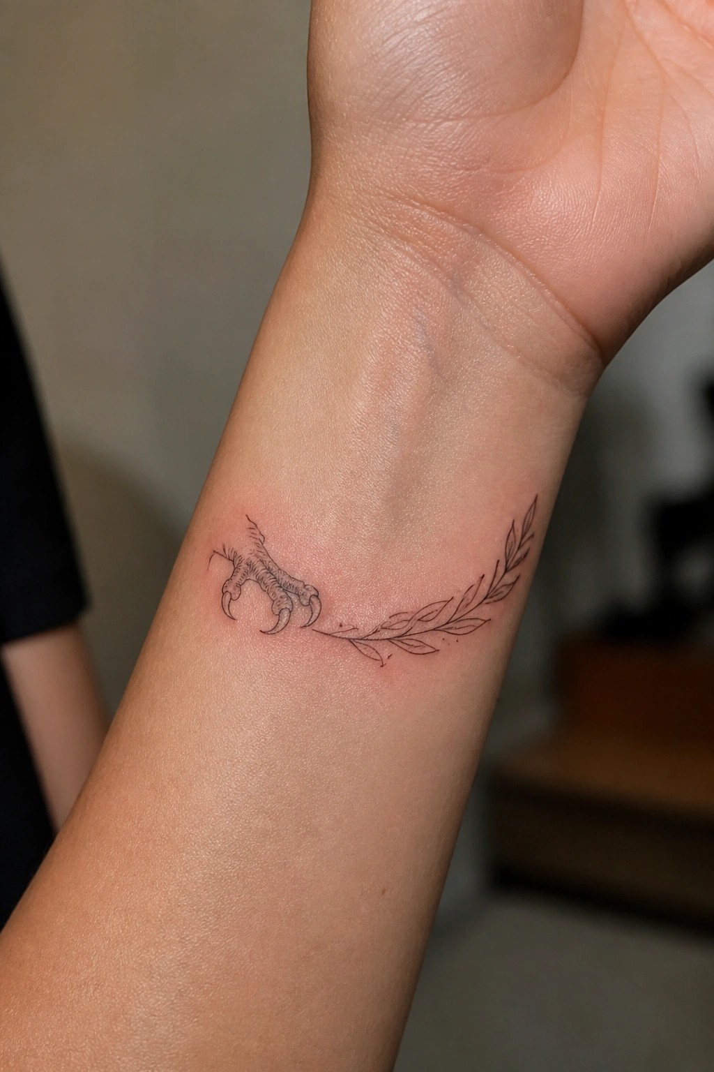 Tattoo of bird talons linked by line to leafy branch on wrist.