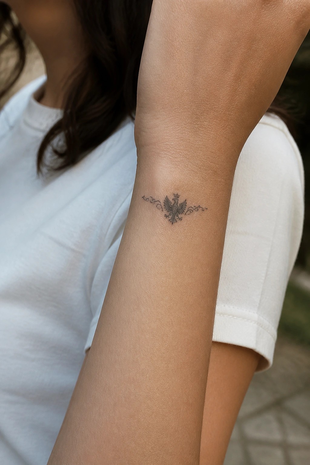 Crowned eagle tattoo with swirls on inner forearm, white shirt sleeve visible.