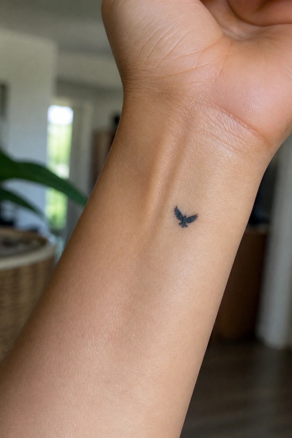 Tiny black bird tattoo on inner wrist of raised hand