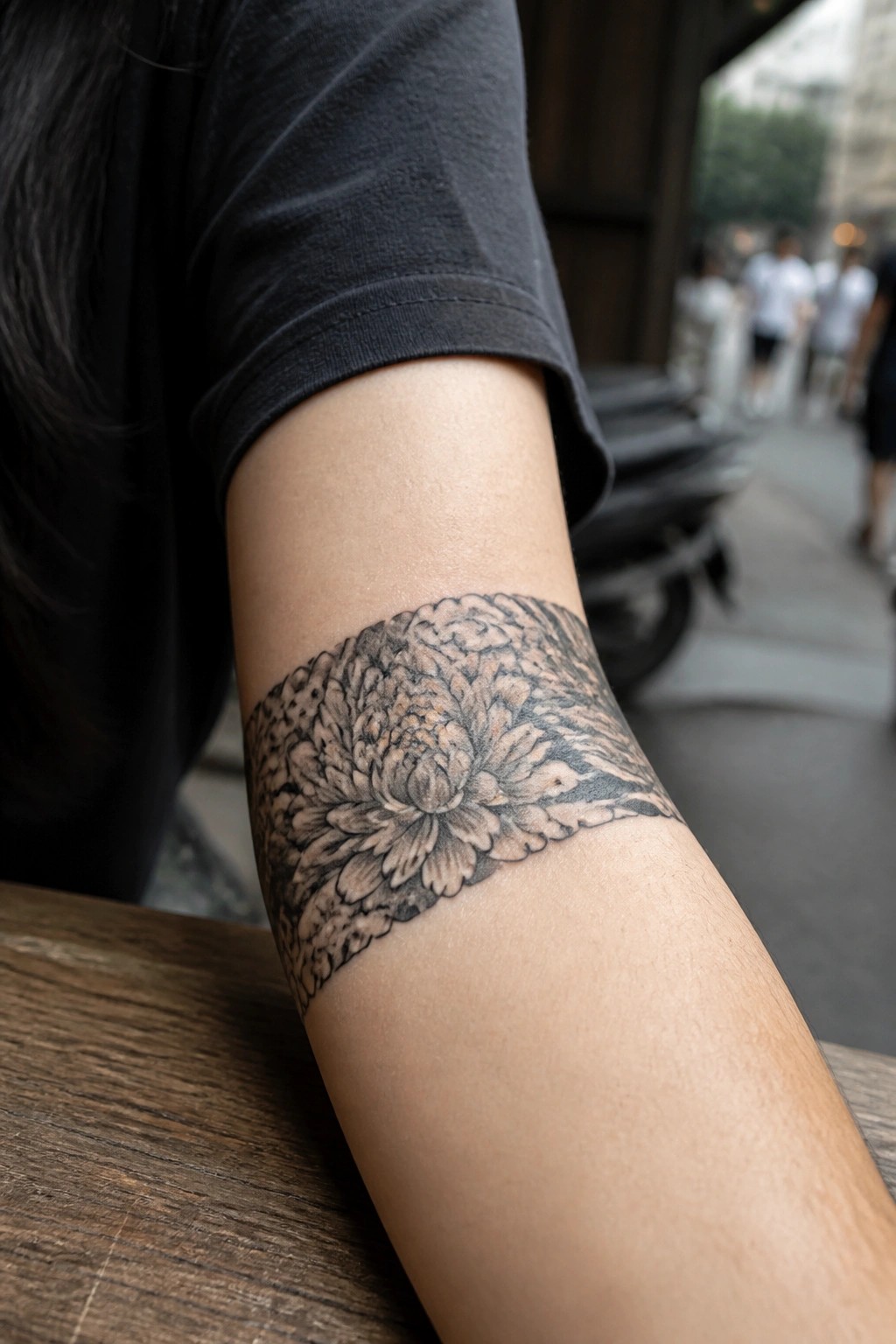 Black-and-gray chrysanthemum tattoo band on forearm under black t-shirt sleeve.