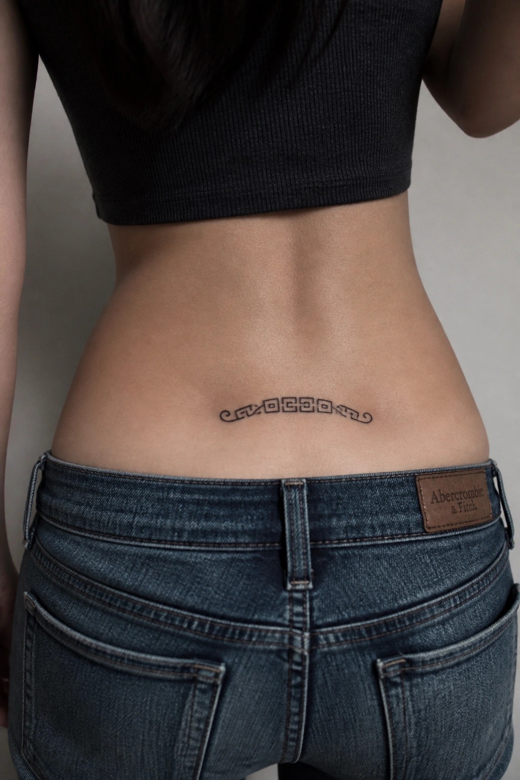 Lower back geometric tattoo above blue jeans and black crop top