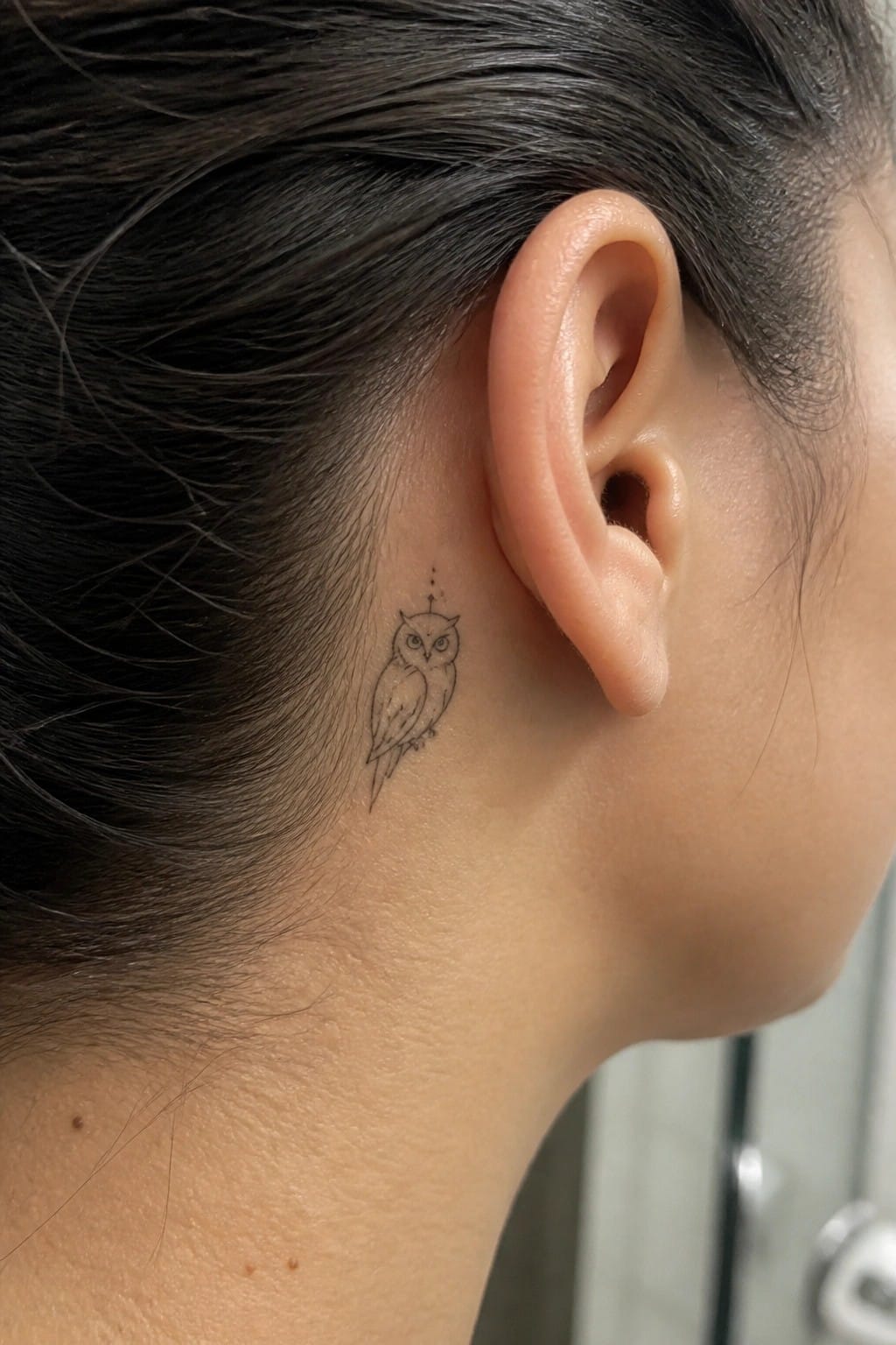 Fine line owl tattoo placed behind the ear on the side of the head