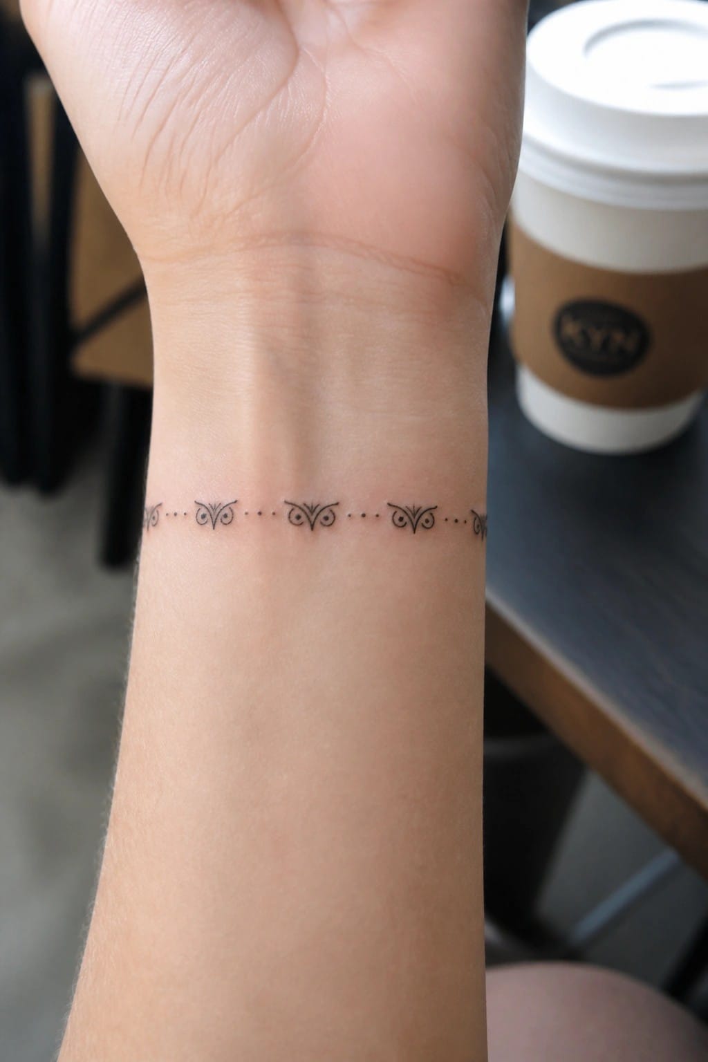 Wrist with delicate dotted tattoo of ornate symmetrical motifs beside white coffee cup