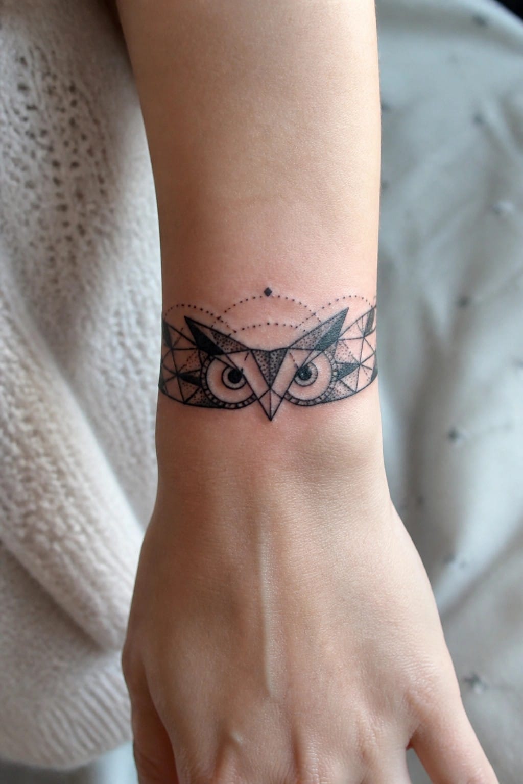 Geometric black owl tattoo on wrist with white knitted sleeve visible