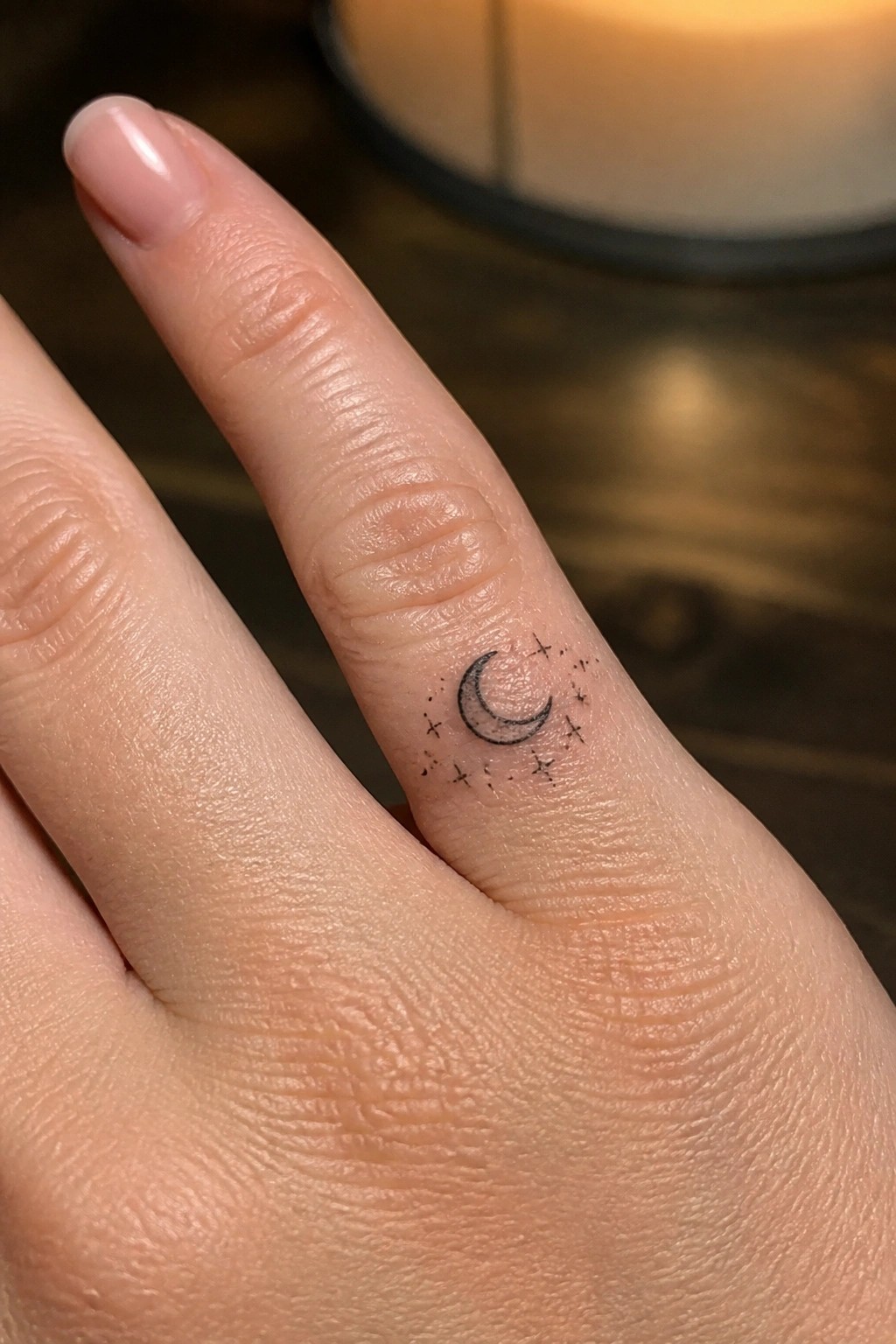 Close-up of ring finger with black crescent moon and stars tattoo, light pink nail.