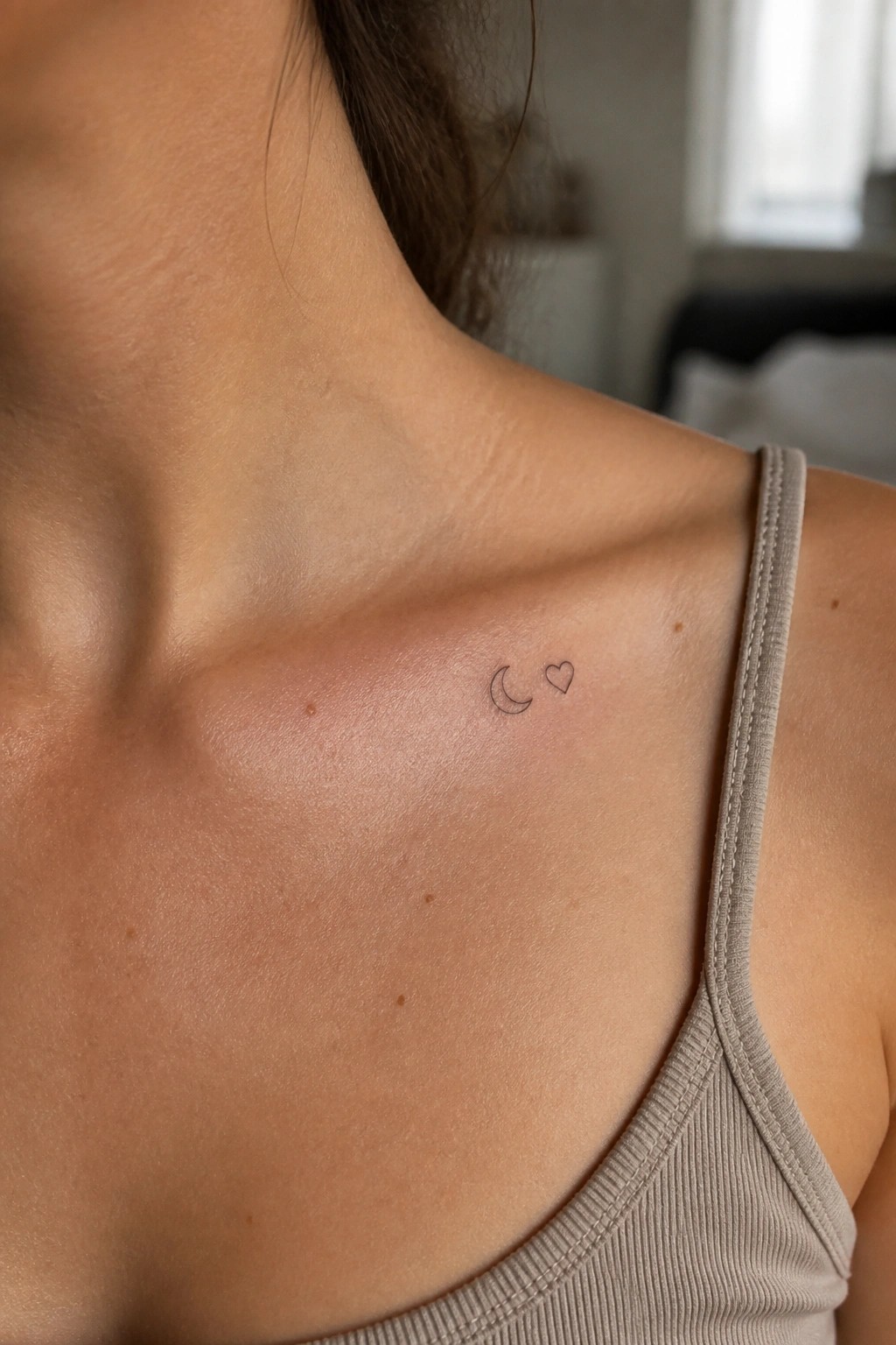 Fine line crescent moon and heart tattoo on a woman's collarbone area