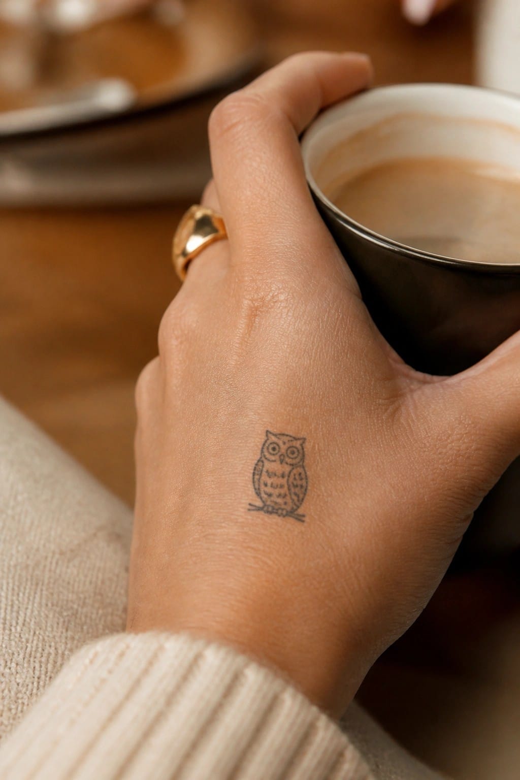 Small minimalist owl tattoo on the back of a hand holding a coffee cup
