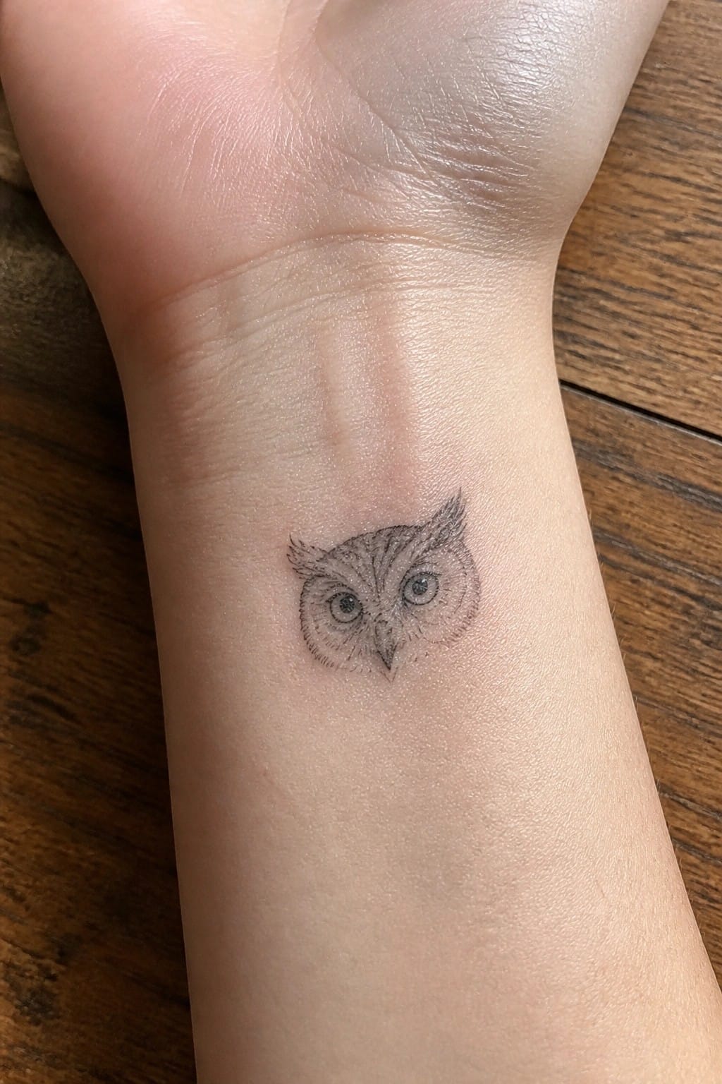 Small black and grey owl tattoo on the inner wrist showing a compact face with fine line details