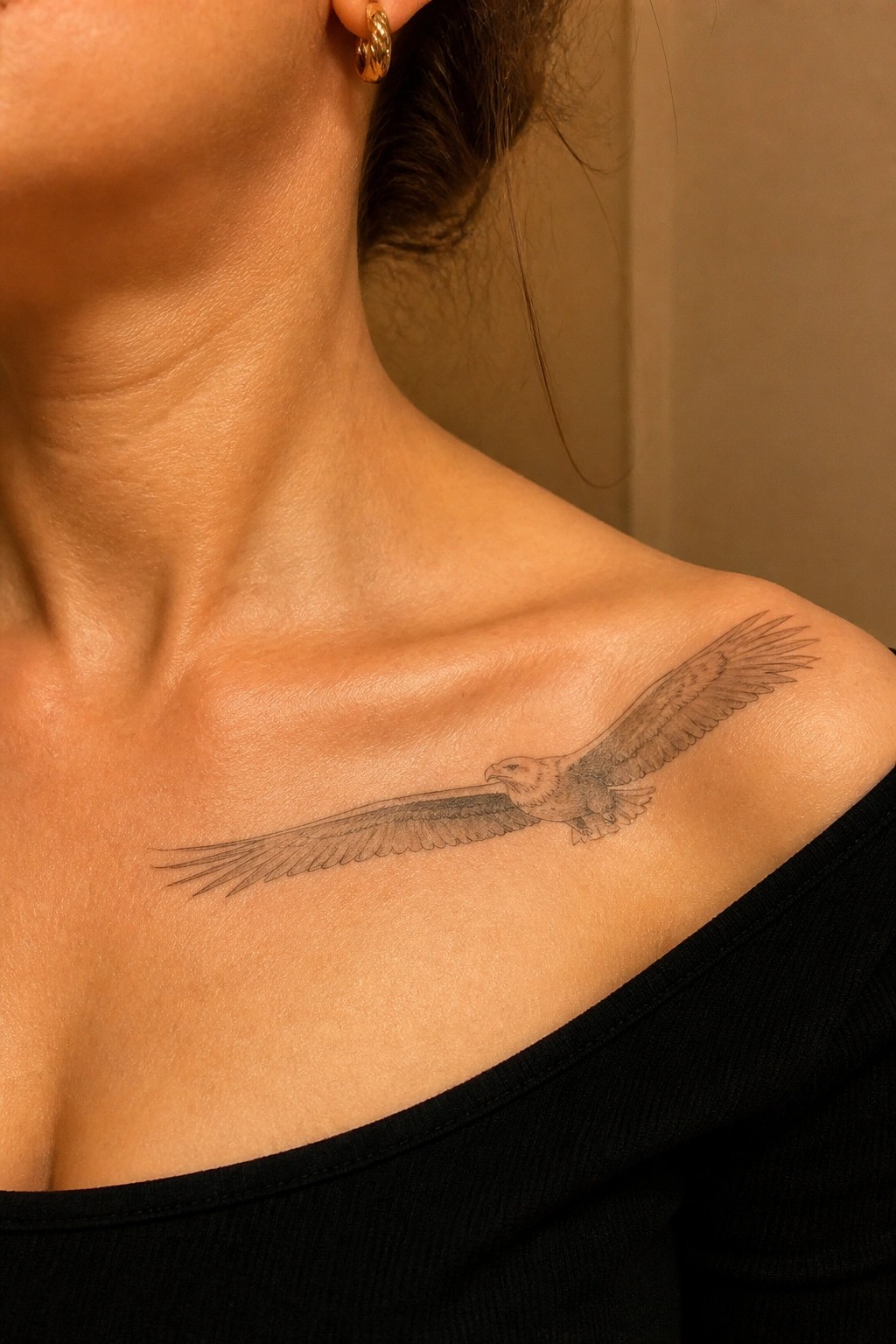 Fine line eagle tattoo placed across the collarbone with wings spread in flight.