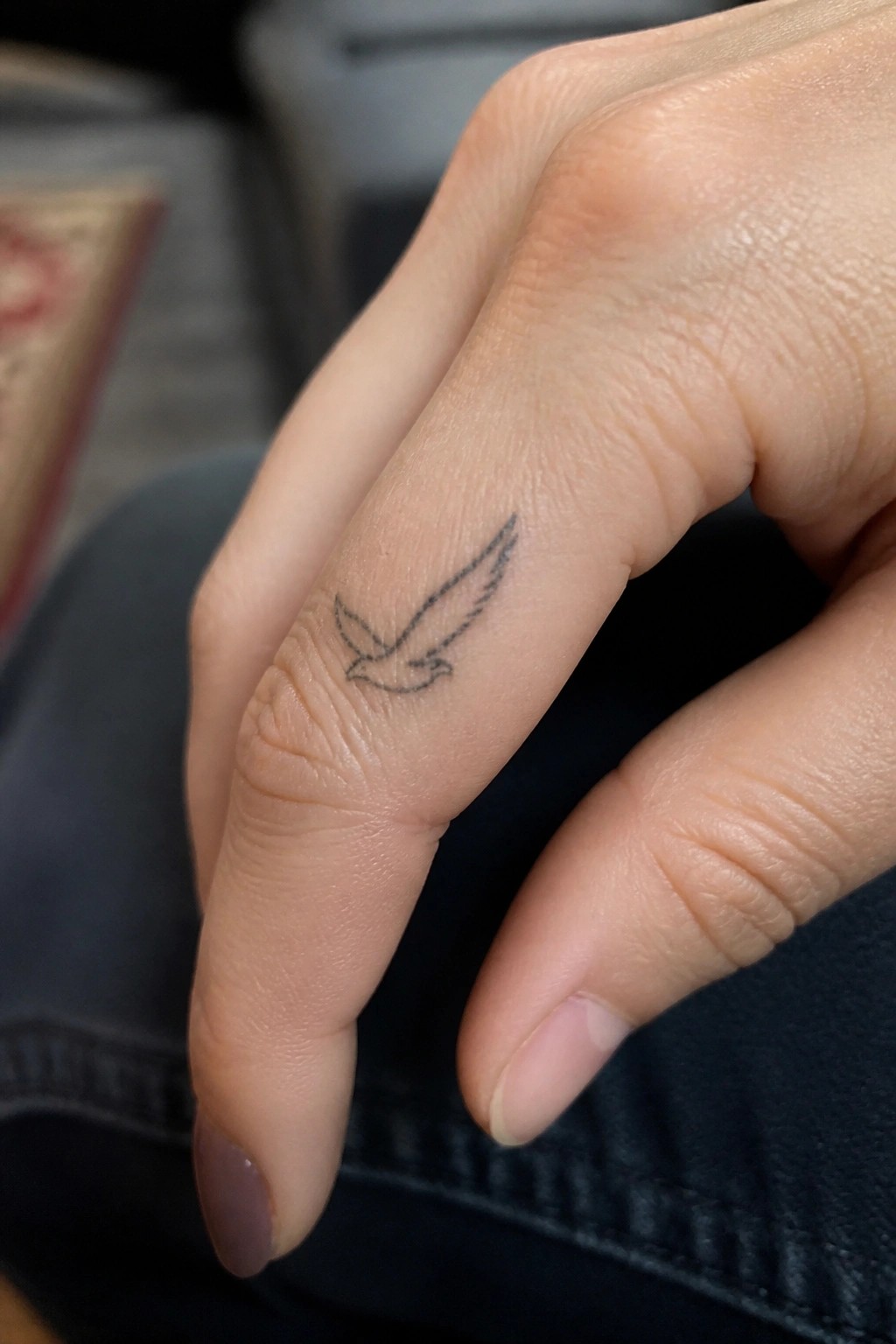 Hand with small black bird tattoo on ring finger over dark fabric