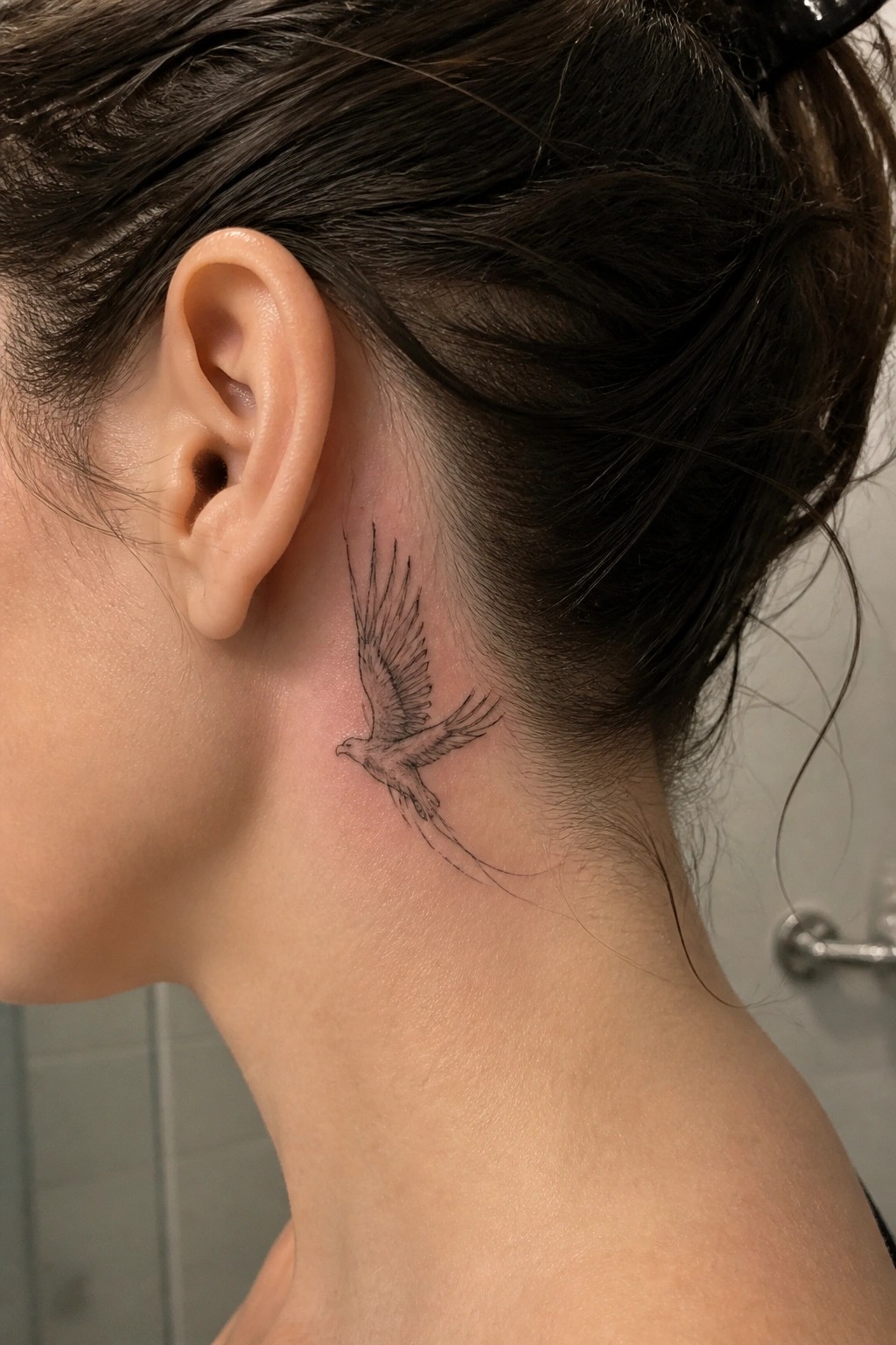 Neck with detailed black bird tattoo behind ear, dark hair pulled back