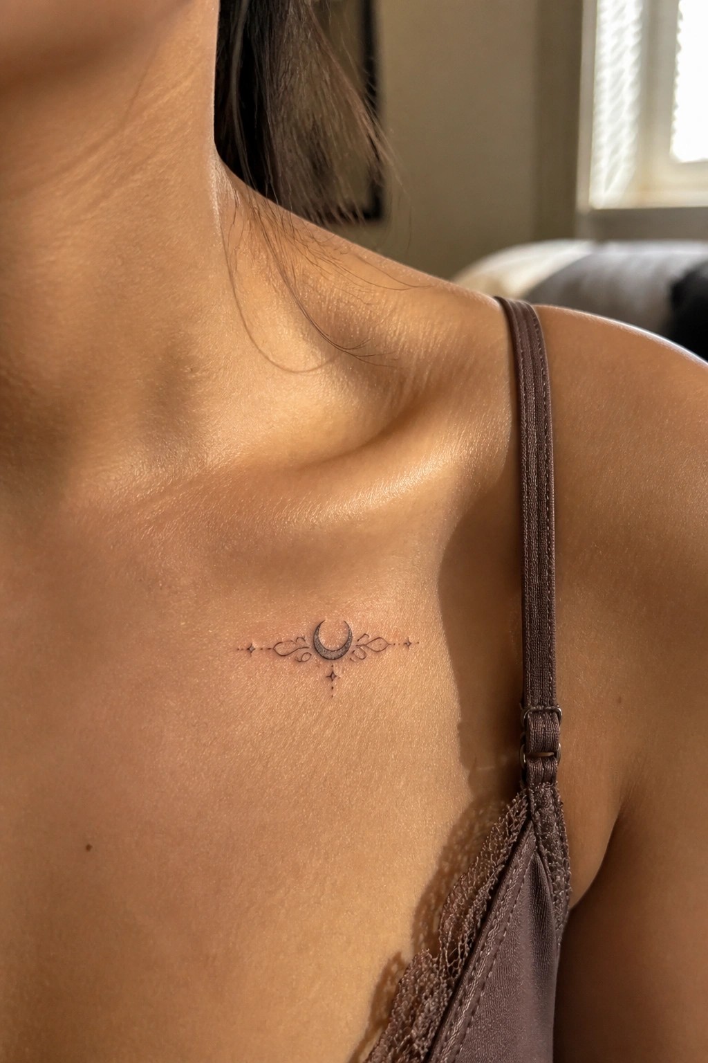 Delicate crescent moon tattoo on collarbone beside brown lace-trimmed tank strap.