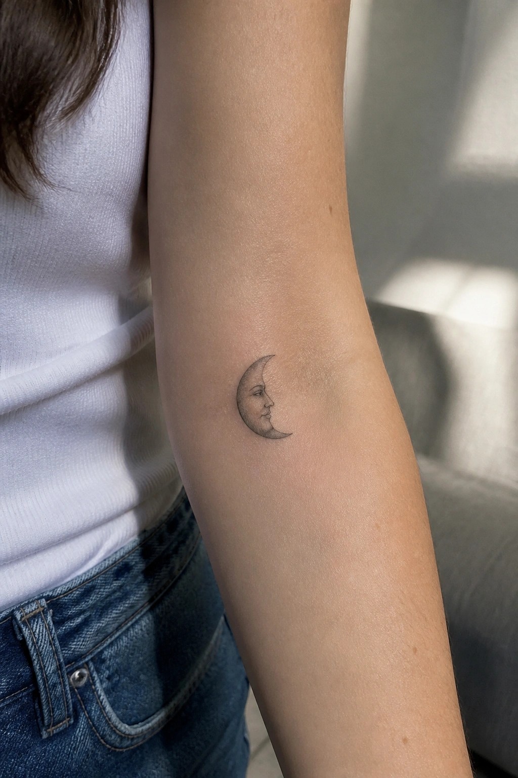 Fine line crescent moon tattoo with a woman's profile on the inner forearm.