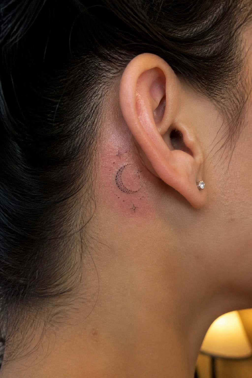 Close-up of ear with crescent moon and stars tattoo plus diamond stud earring