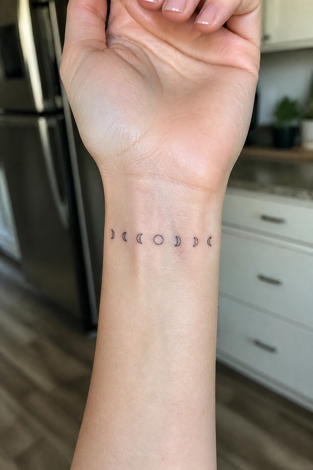 Moon phase tattoo on inner wrist of raised hand in kitchen