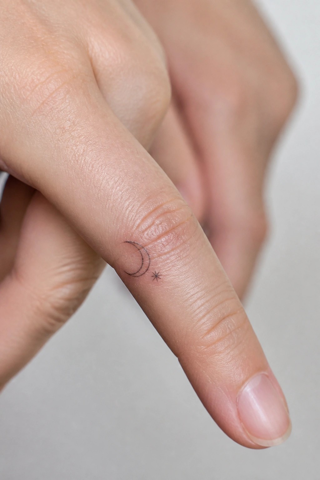 Minimalist crescent moon and star tattoo placed on the side of a finger